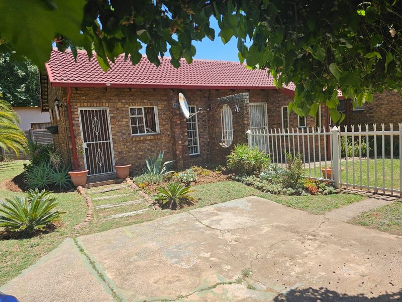Front view of a face brick house featuring a tiled roof, security gates, and a concrete driveway with established garden beds.