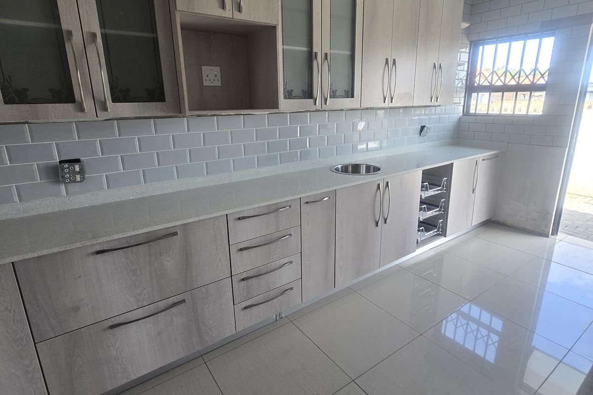 Modern kitchen featuring light wood-grain cabinetry, quartz countertops, subway tile backsplash, and polished porcelain floor tiles in a clean, empty space.