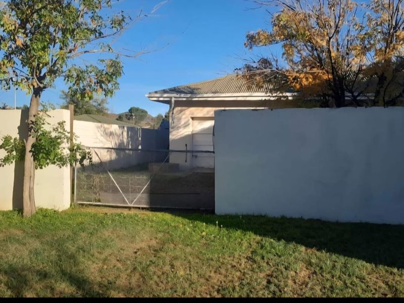 A view of the rear exterior area featuring a perimeter wall, metal gate, and access to a garage with a tiled roof.