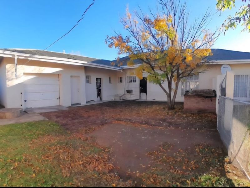 Rear view of the property featuring a single garage, paved driveway area, and surrounding perimeter walling with established garden space.