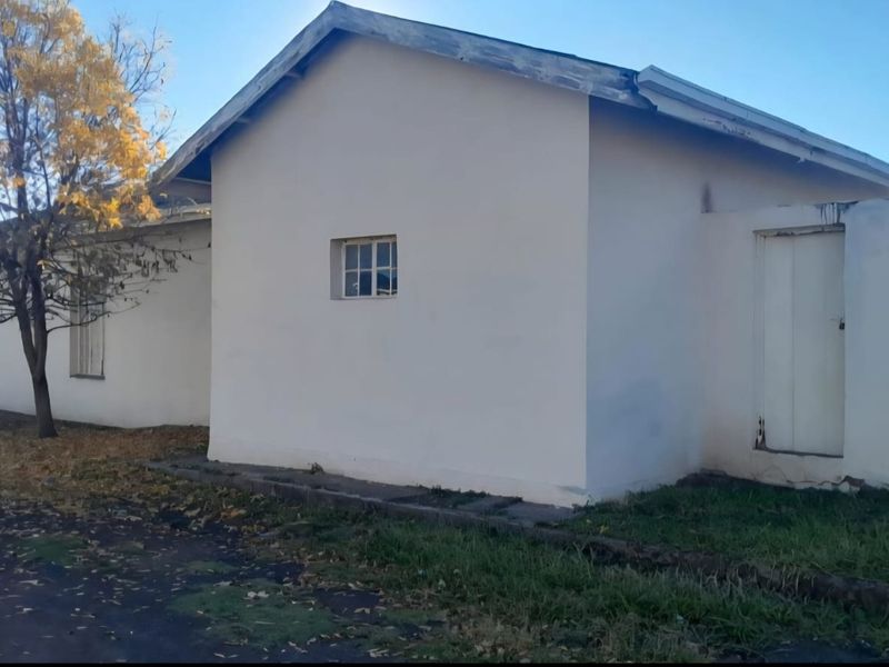 Side view of a residential property showing a simple facade with a pitched roof, small pane window, and a side entrance door.