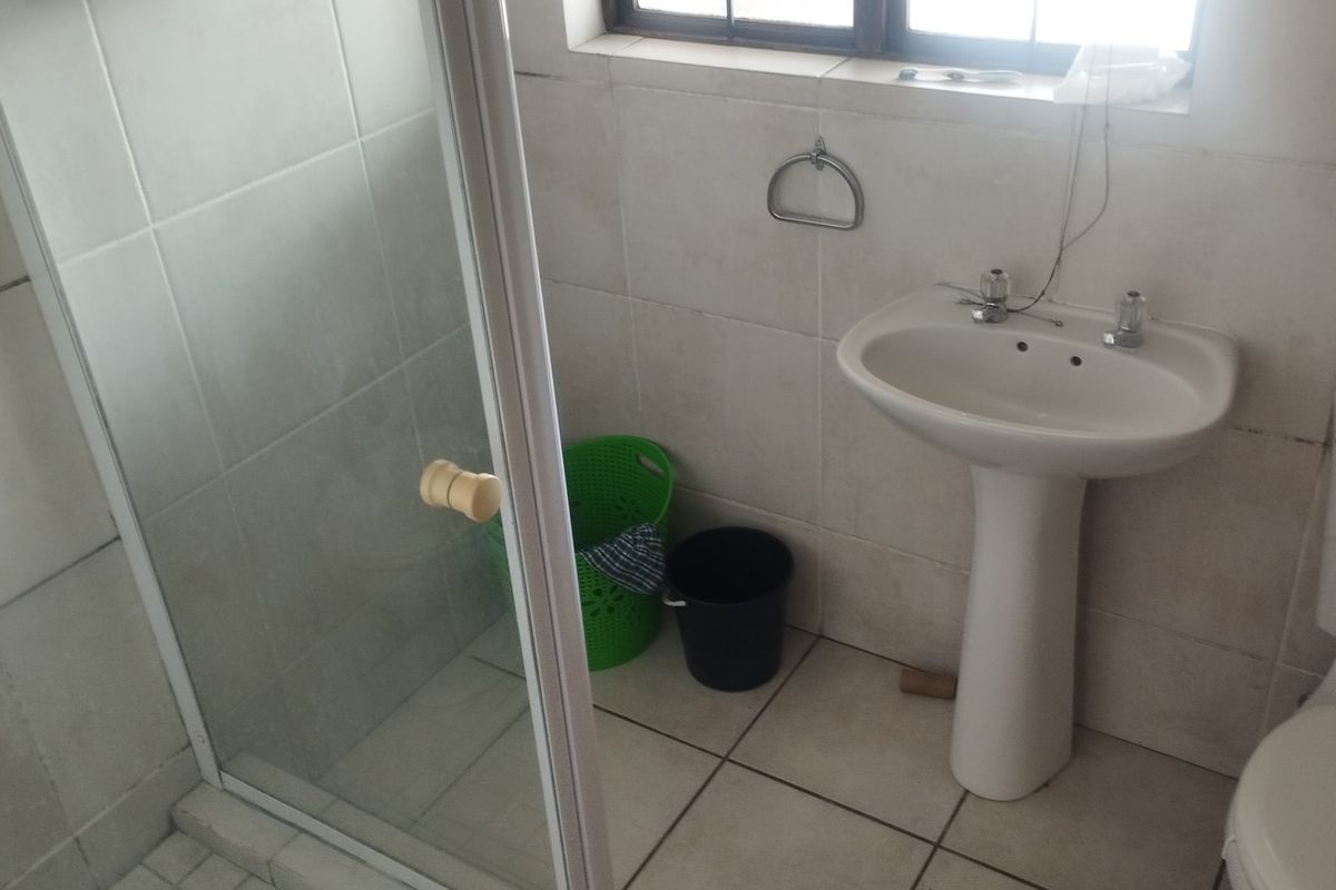 A functional bathroom featuring a pedestal basin, toilet, and a glass-enclosed shower with neutral wall and floor tiling.
