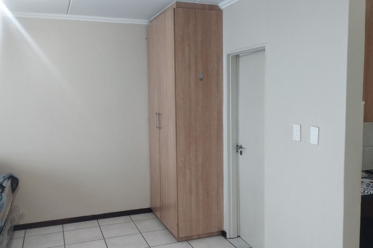 A bedroom featuring light-toned built-in cupboards, tiled flooring, and a neutral wall finish, providing a functional and clean living space.