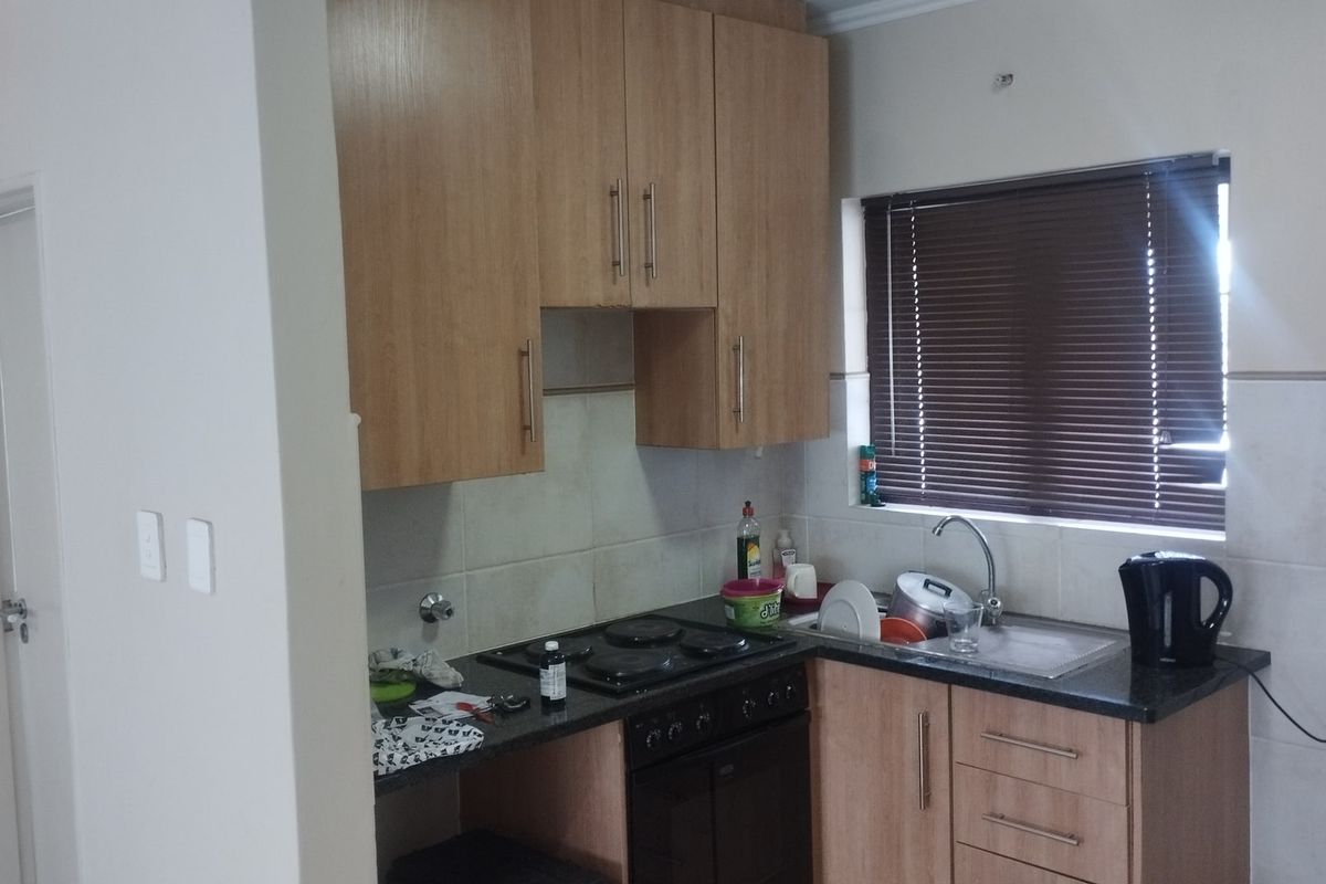 A functional kitchen featuring light wood-finish cabinetry, granite countertops, a built-in electric hob and oven, and a stainless steel sink with tiled splashbacks.