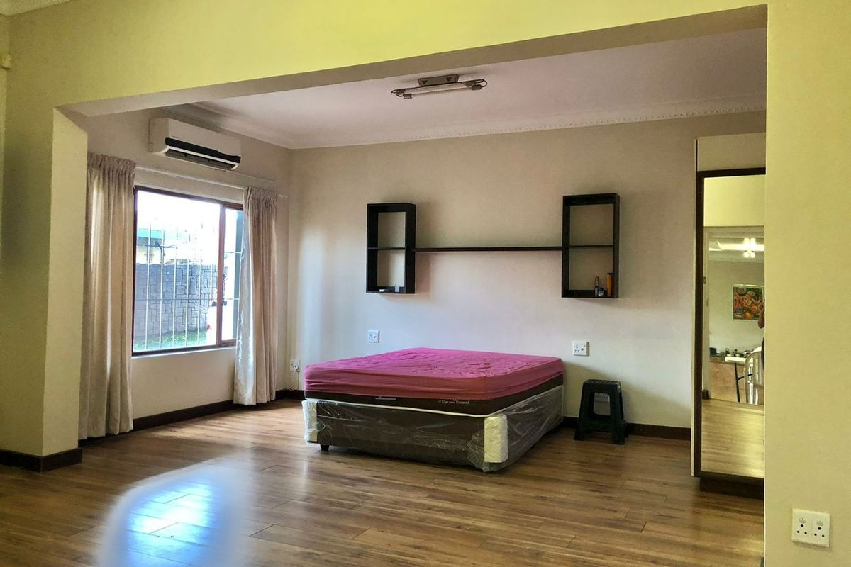 Spacious bedroom featuring laminate flooring, built-in shelving, and a wall-mounted air conditioning unit.