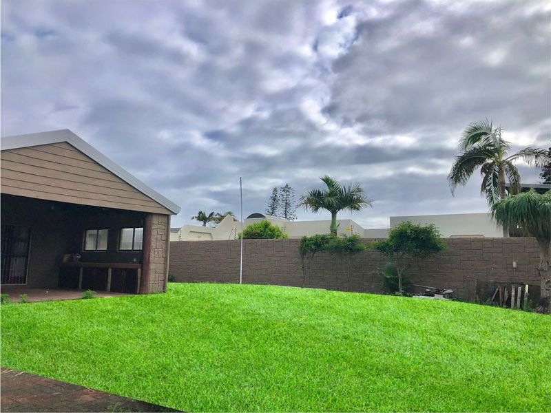 A spacious rear garden featuring a well-maintained lawn, a covered patio area with a built-in braai, and secure perimeter walling with electric fencing.