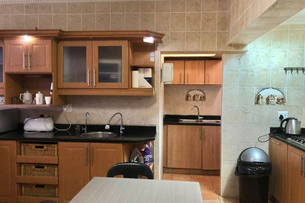 A functional kitchen featuring wooden cabinetry, granite countertops, and a tiled backsplash, with an adjoining scullery area for additional prep and storage space.