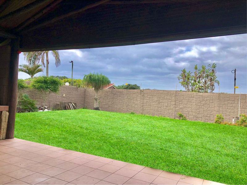 A covered patio area overlooking a private garden with a well-maintained lawn and secure perimeter walling.