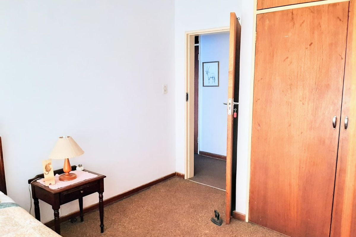 A bedroom featuring built-in wooden cupboards and carpeted flooring, providing a functional space with potential for cosmetic updates.
