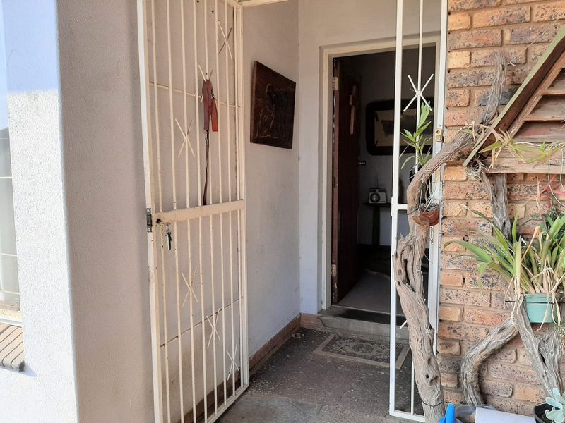 A residential entrance featuring a white security gate, brick exterior wall, and a timber front door leading into the home.