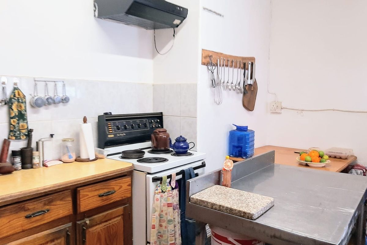A functional kitchen featuring wooden cabinetry, a freestanding stove with an extractor fan, and a stainless steel prep table with tiled splashbacks.