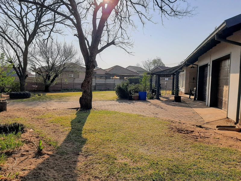 Spacious rear garden featuring a paved patio area with a pergola, established trees, and a double garage with direct access to the yard.