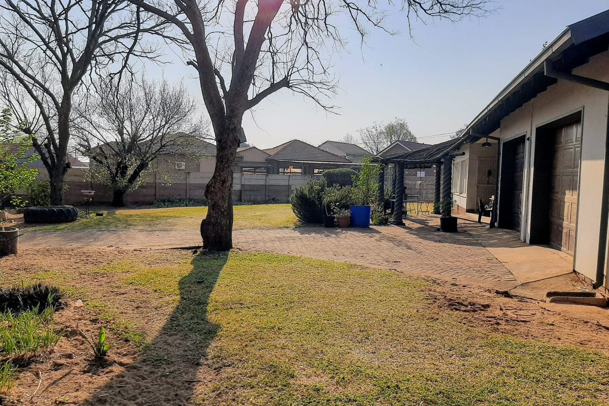 Spacious rear garden featuring a paved patio area with a pergola, established trees, and a double garage with direct access to the yard.