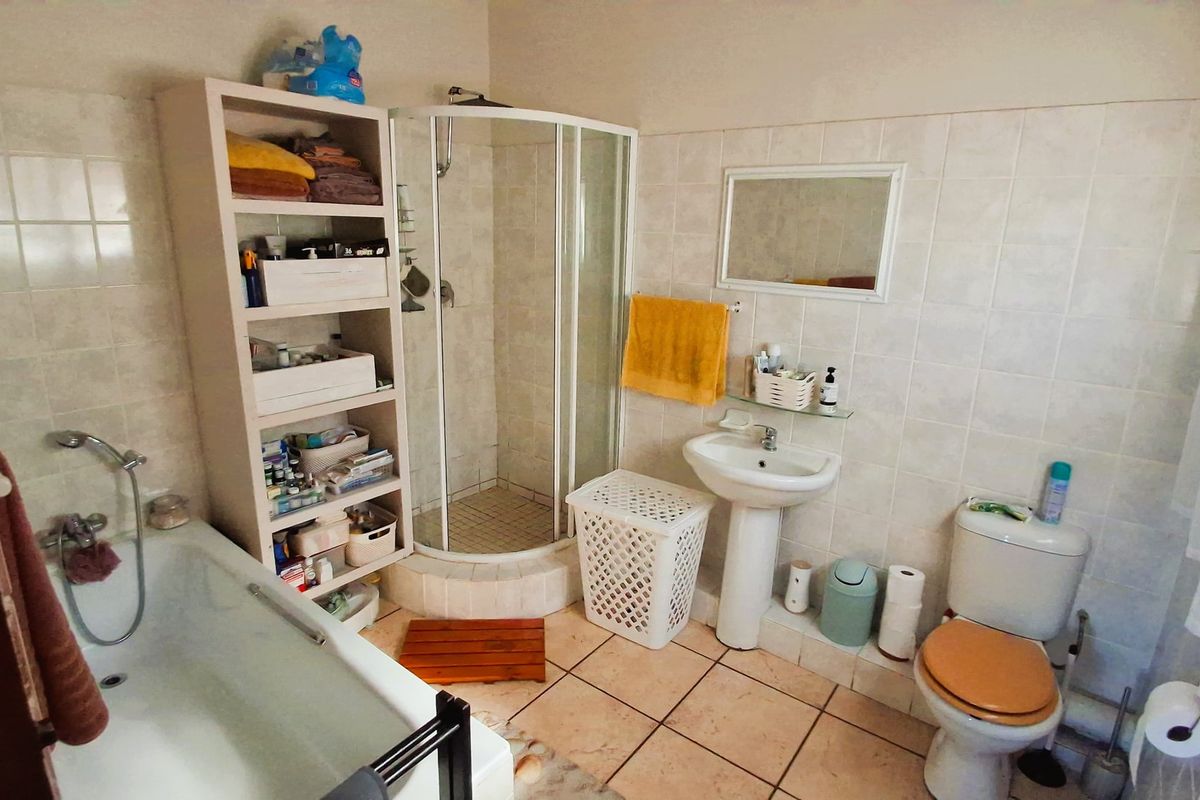 A functional bathroom featuring a shower enclosure, bathtub, pedestal basin, and toilet with neutral wall and floor tiling.
