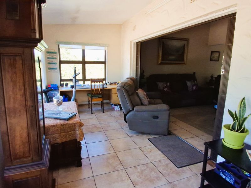 A living area featuring tiled flooring and a sliding room divider, connecting to an adjacent space with natural light from a large window.