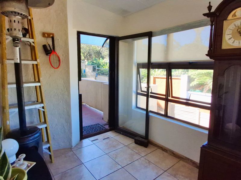 A sunlit enclosed patio area featuring tiled flooring, aluminium sliding doors, and large windows with roller blinds, providing direct access to the outdoor space.