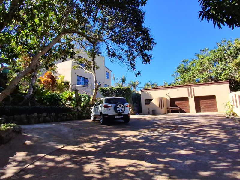 Front exterior view of the property featuring a paved driveway, double garage, and established garden surroundings.