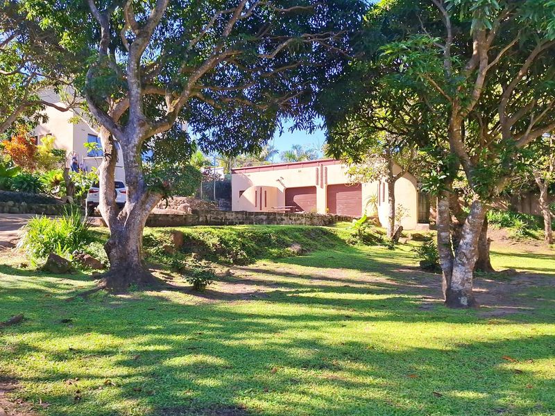 A view of the property's front exterior, featuring a double garage, paved driveway, and a spacious, mature garden setting.