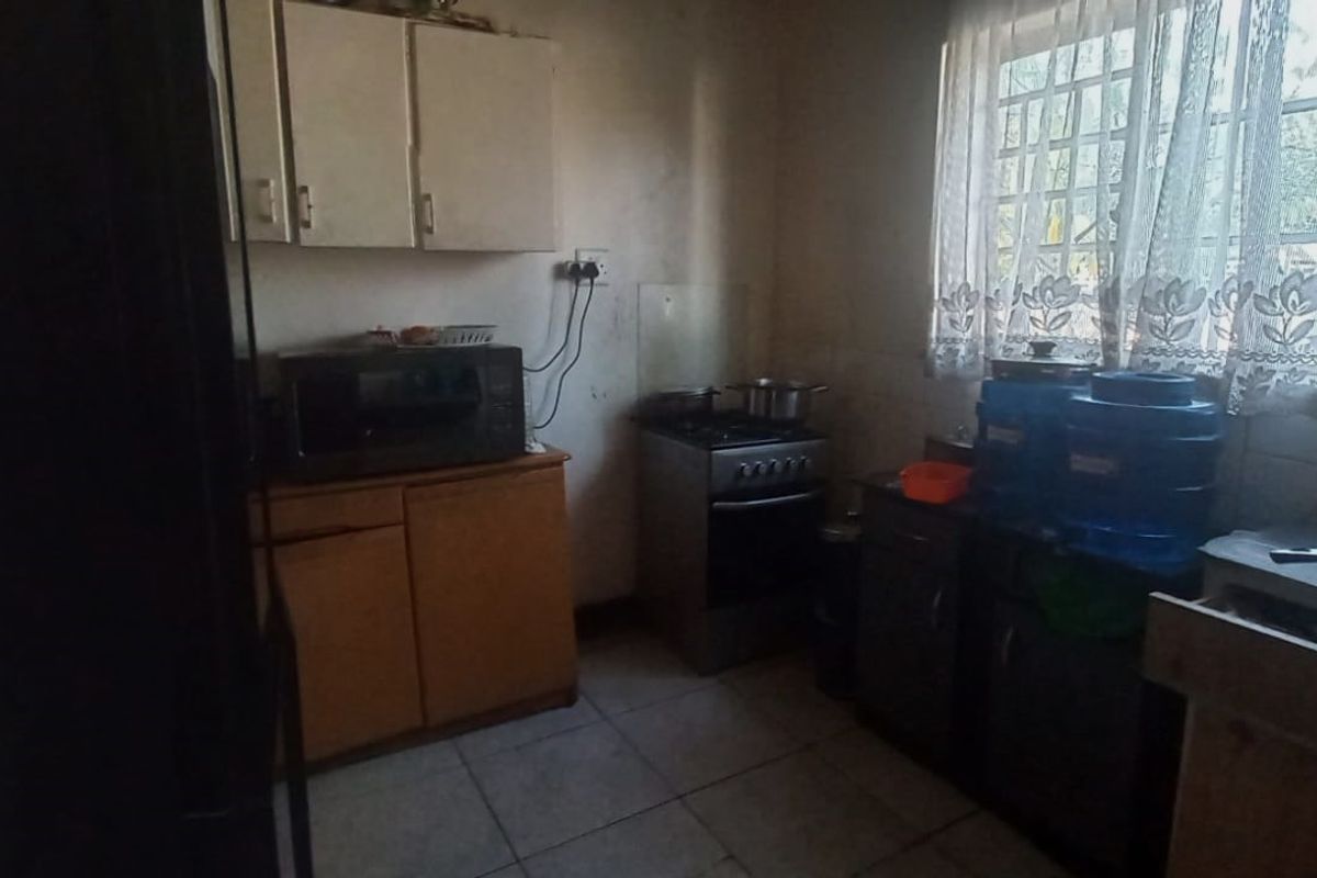 A dated kitchen featuring built-in cabinetry, tiled flooring, and a freestanding stove, requiring cosmetic updates to modernize the space.