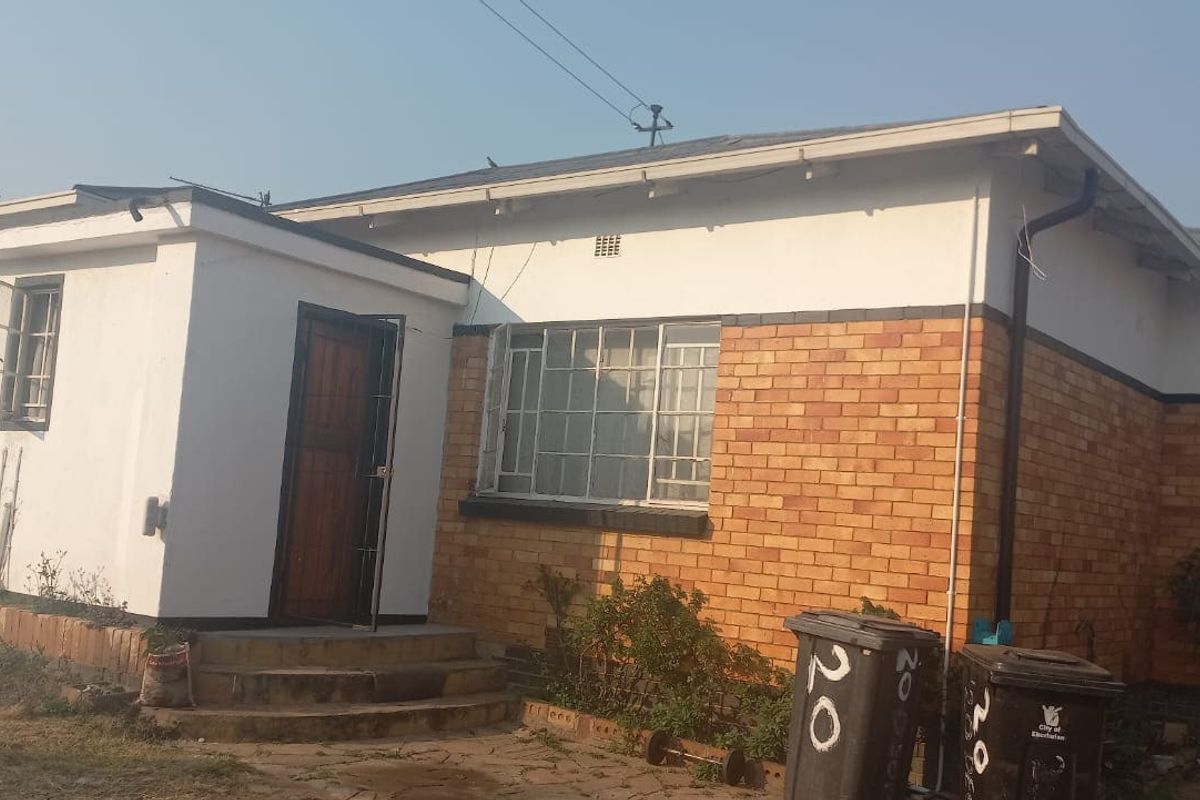 Rear view of a single-story brick house featuring metal window frames, a security gate, and concrete steps leading to the entrance.