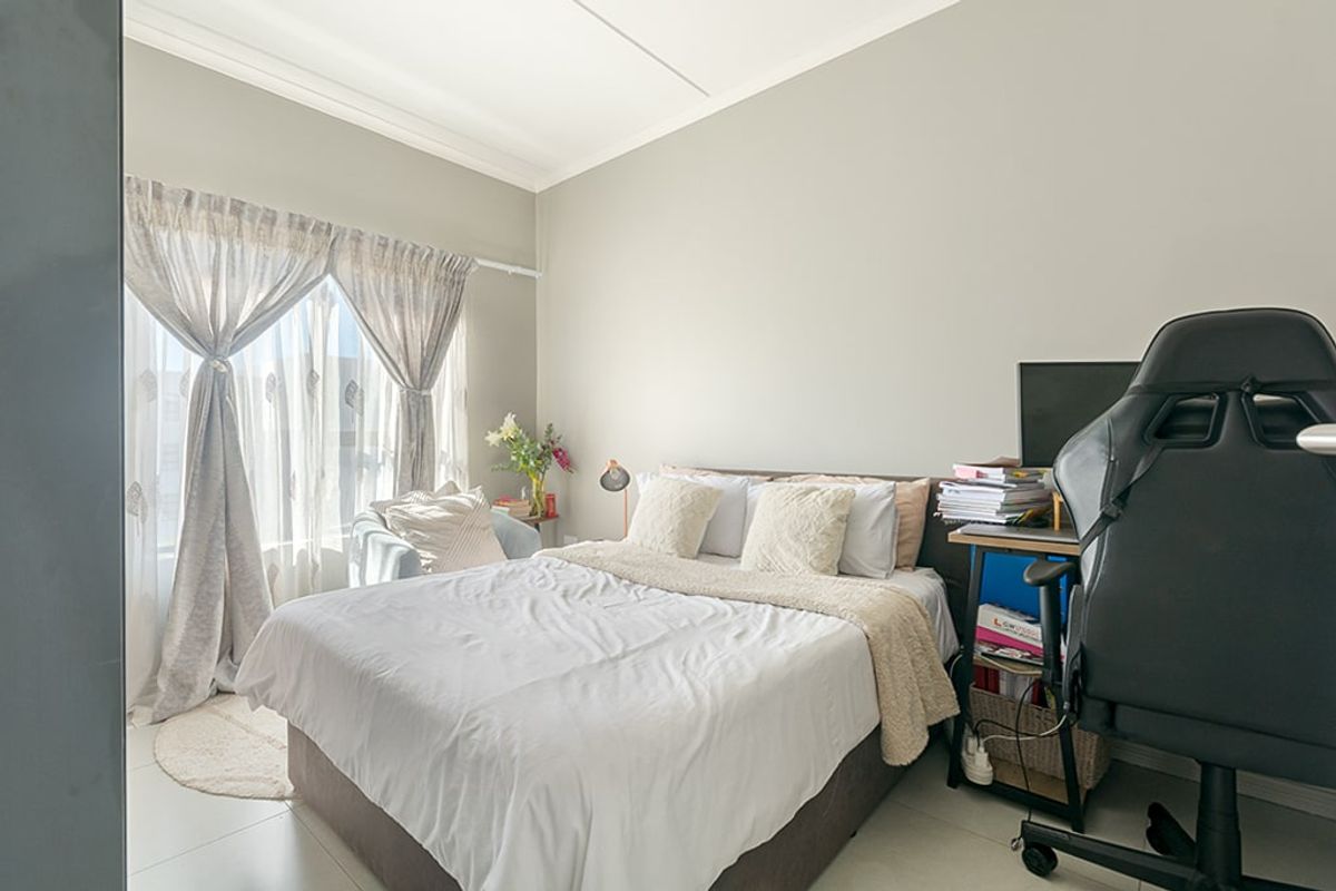 A well-lit bedroom featuring neutral wall tones, tiled flooring, and large windows with curtain rails, providing a comfortable and functional living space.