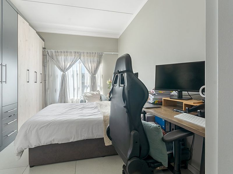 A well-maintained bedroom featuring built-in wardrobes and tiled flooring, currently utilized as a combined sleeping and workspace area.