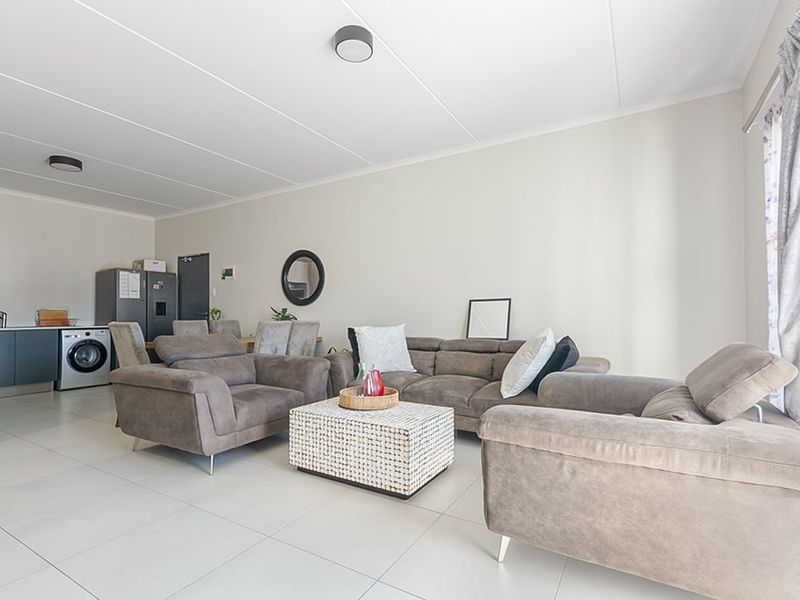 A bright open-plan living area featuring neutral tiled flooring, modern kitchen cabinetry with integrated laundry appliances, and a spacious, well-lit layout.