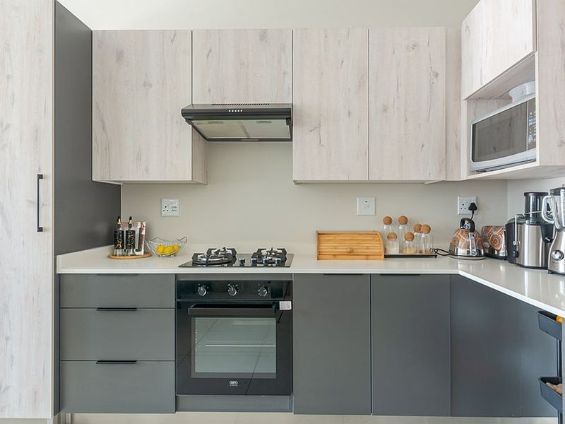 Modern kitchen featuring two-tone cabinetry, stone countertops, integrated oven, gas hob, and built-in microwave, offering a clean and functional cooking space.