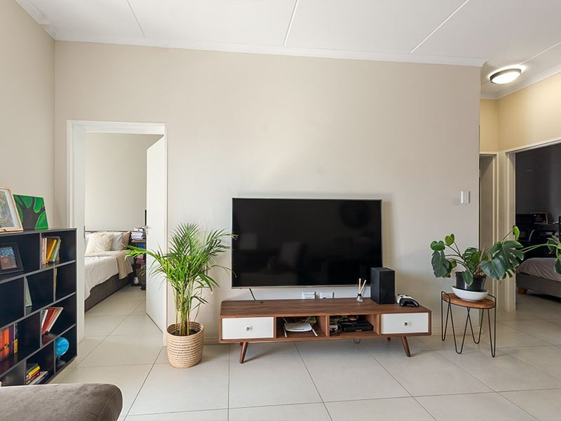 A bright living room featuring neutral walls, tiled flooring, and access to adjacent bedrooms.