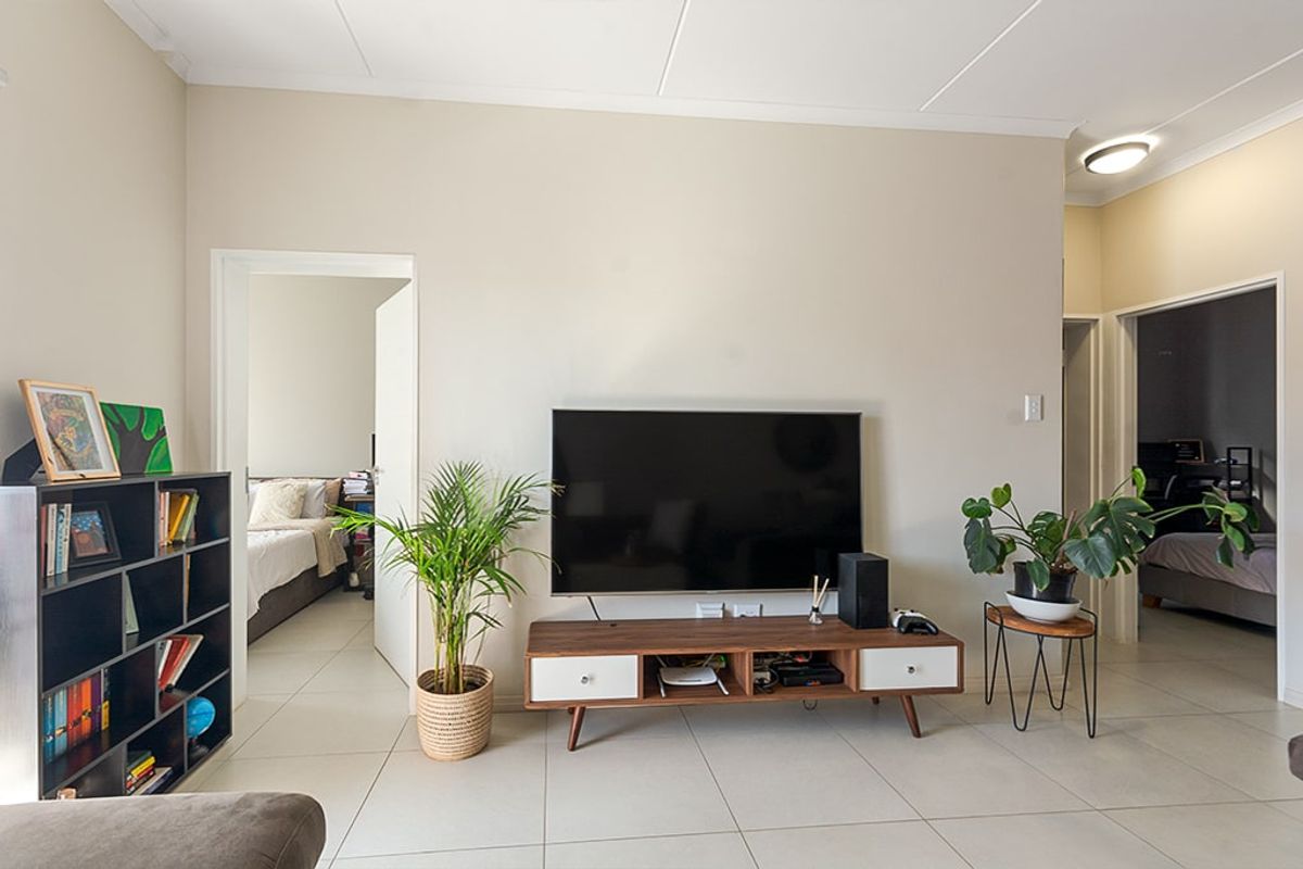 A bright living room featuring neutral walls, tiled flooring, and access to adjacent bedrooms.