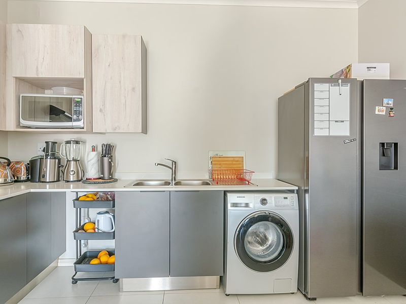 A modern kitchen featuring light wood-grain upper cabinets, dark grey lower cabinetry, a stainless steel sink, and integrated space for laundry appliances.