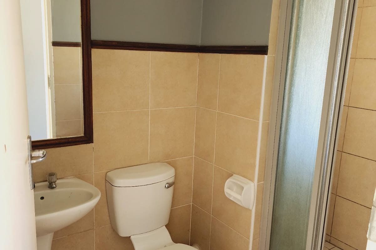 A functional bathroom featuring a pedestal sink, a standard toilet, and a corner shower enclosure with tiled walls and flooring.