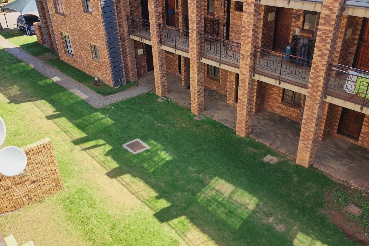 Elevated view of a multi-story apartment complex featuring face-brick facade, private balconies with metal railings, and a shared communal lawn area.