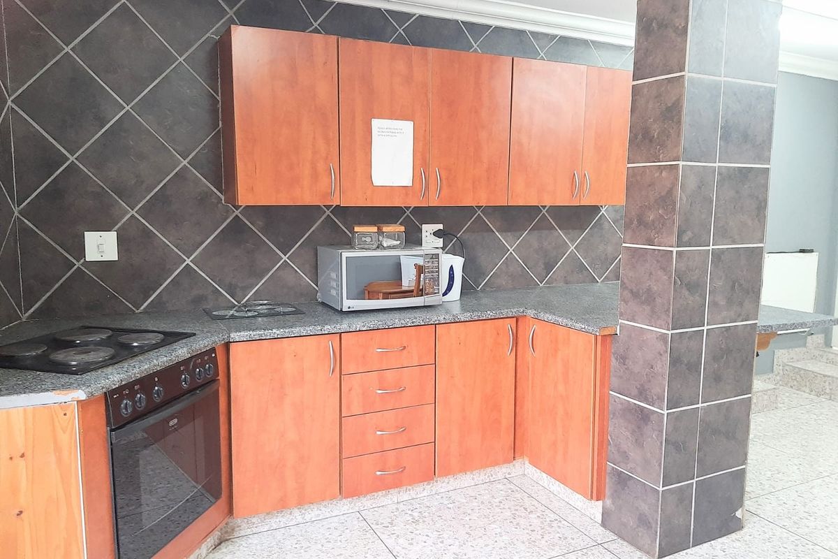 A functional kitchen featuring wooden cabinetry, granite-look countertops, a built-in oven and hob, and dark tiled splashbacks.