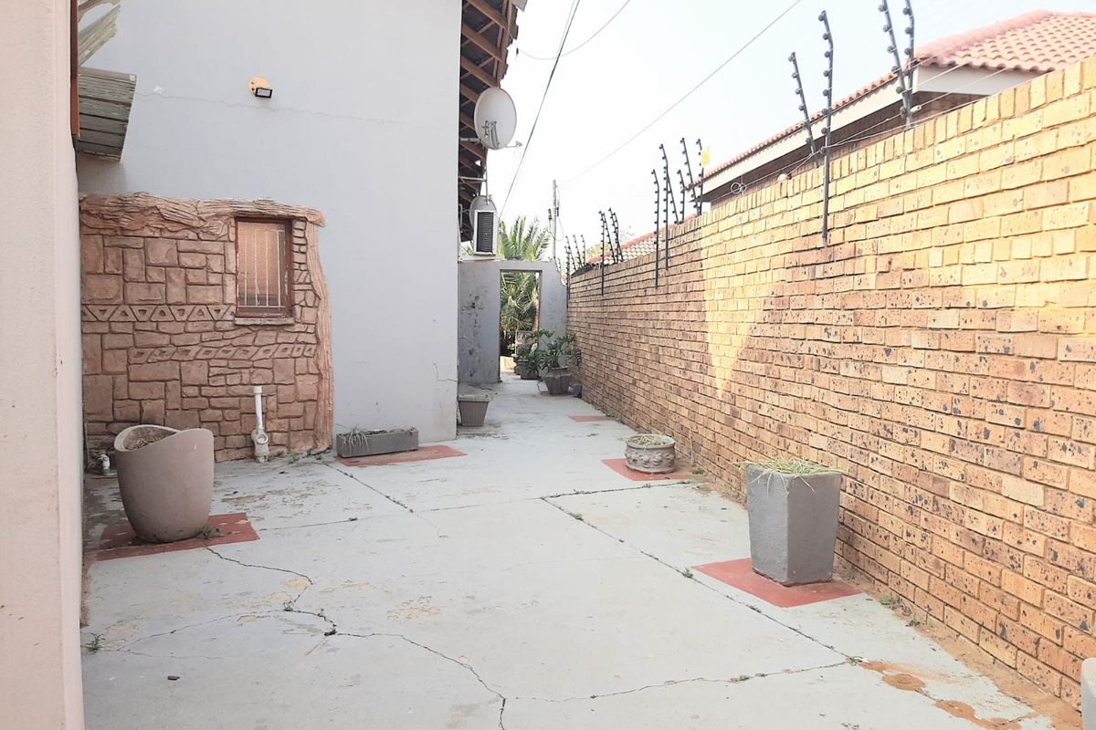 A side exterior walkway featuring a brick boundary wall with electric fencing and concrete paving.