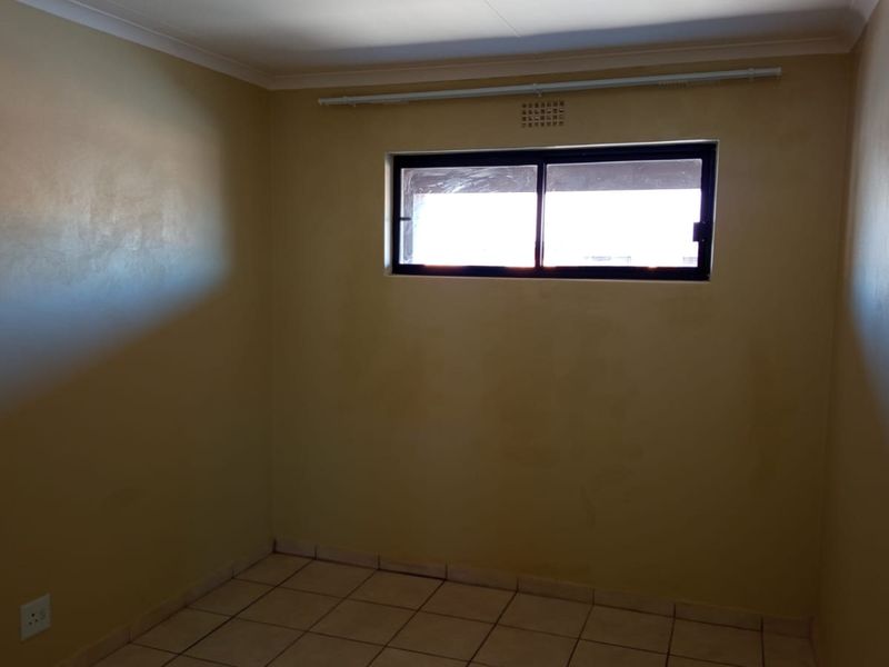 An empty bedroom featuring tiled flooring, a horizontal sliding window with a curtain rail, and neutral wall finishes.