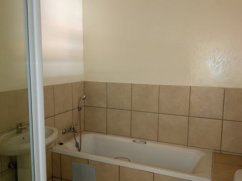 A functional bathroom featuring a bathtub, pedestal basin, and a separate shower enclosure with neutral wall tiling.