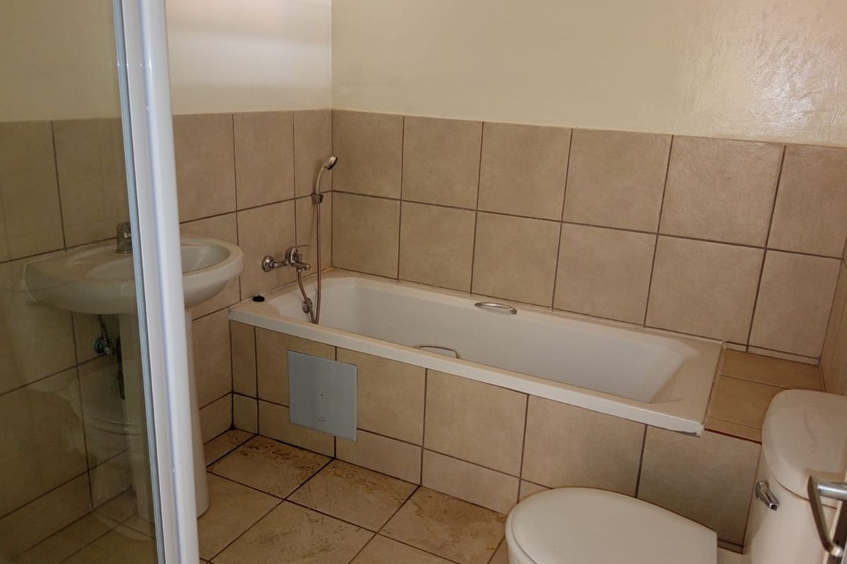 A functional bathroom featuring a bathtub, separate shower enclosure, pedestal basin, and toilet with neutral wall and floor tiling.