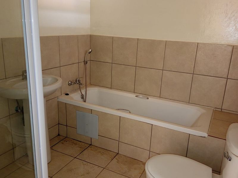 A functional bathroom featuring a bathtub, separate shower enclosure, pedestal basin, and toilet with neutral wall and floor tiling.