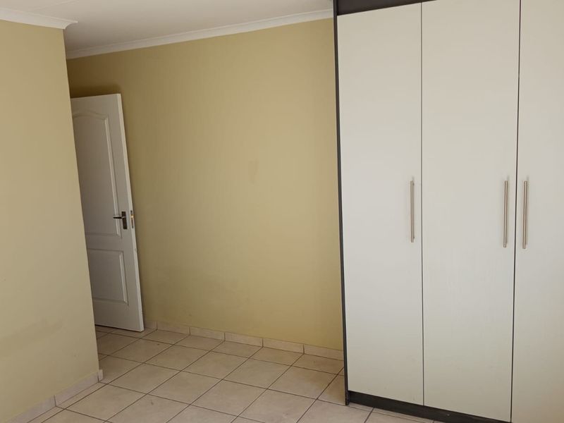 An empty bedroom featuring tiled flooring and a large built-in wardrobe with modern handles.