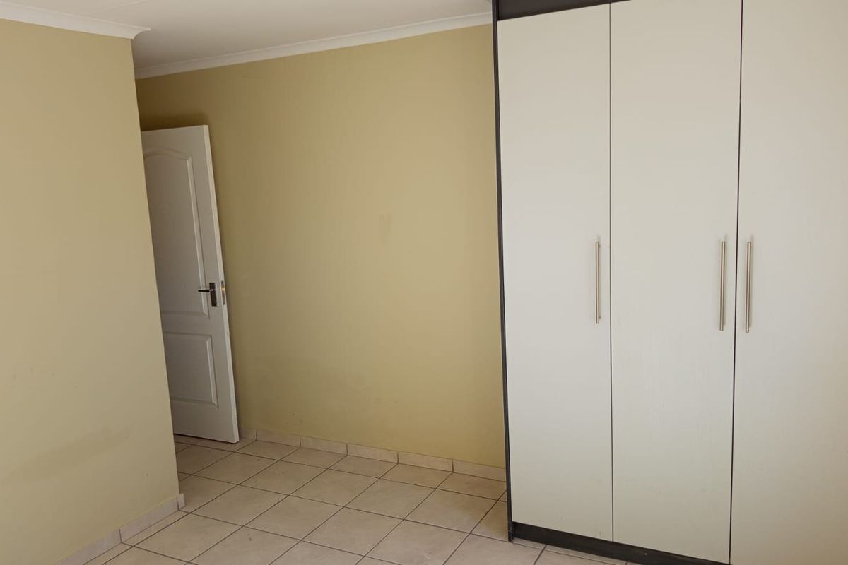 An empty bedroom featuring tiled flooring and a large built-in wardrobe with modern handles.
