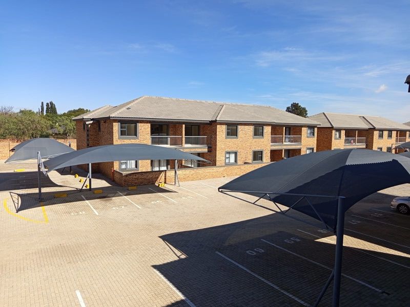 Exterior view of a brick apartment complex featuring paved parking bays with shade cloth carports and private balconies.