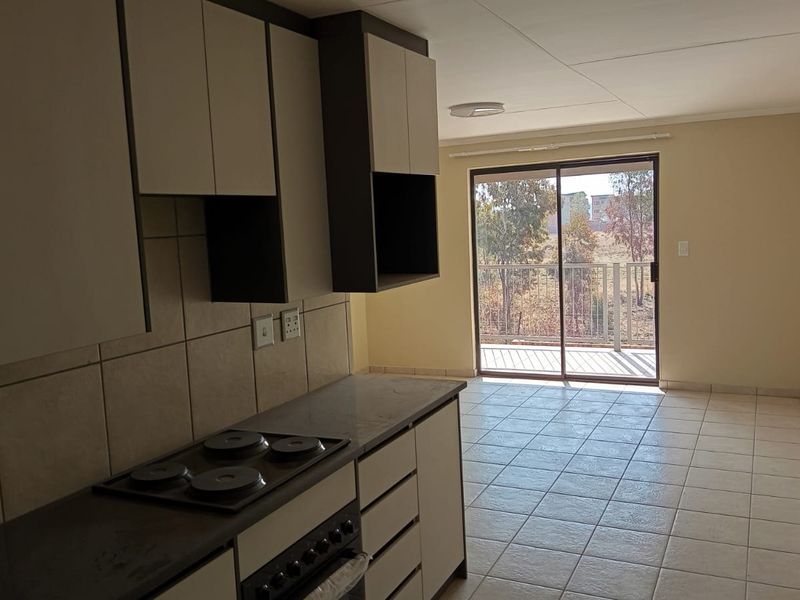 Open-plan kitchen and living area featuring tiled flooring, built-in cabinetry with an electric hob, and a sliding door leading to a balcony.