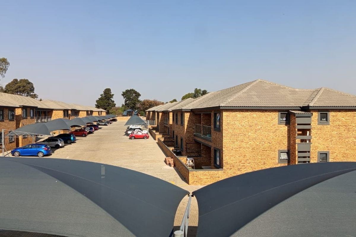 An elevated view of an apartment complex featuring face brick buildings, tiled roofs, and designated shade cloth parking bays for residents.