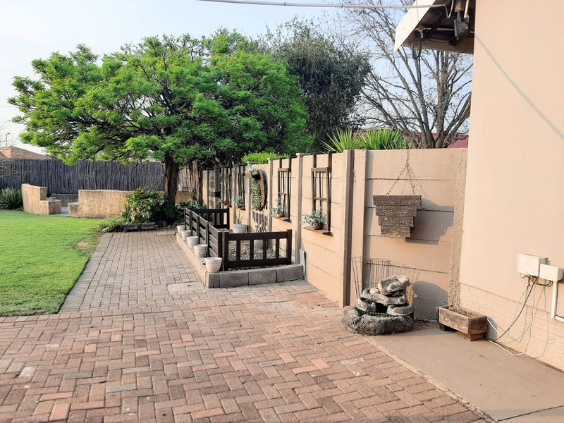 A rear garden area featuring a paved patio, a raised garden bed, and a mature tree set against a precast concrete boundary wall.