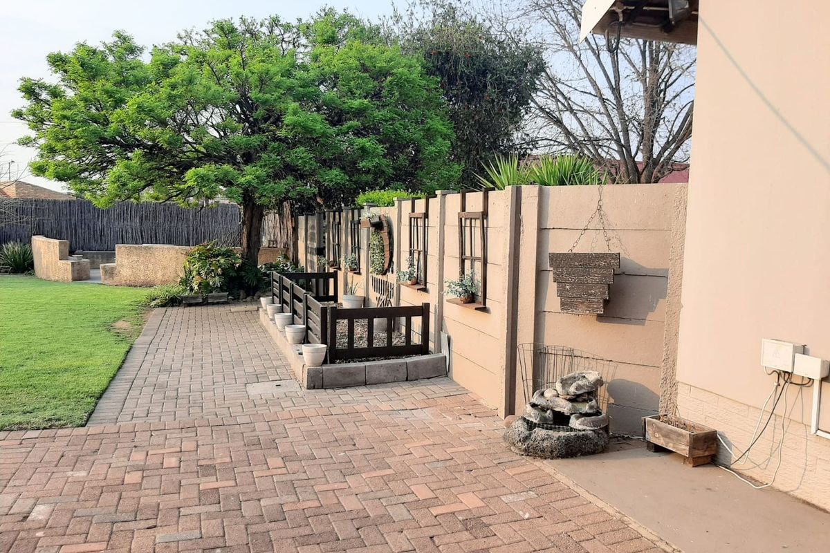 A rear garden area featuring a paved patio, a raised garden bed, and a mature tree set against a precast concrete boundary wall.