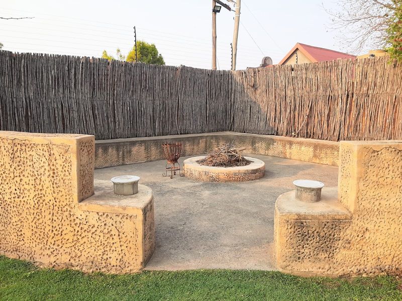 Outdoor entertainment area featuring a built-in circular fire pit and integrated concrete seating, enclosed by rustic reed fencing.