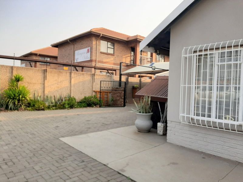 A view of the property exterior featuring a paved driveway, secure perimeter wall with electric fencing, and a residential building with security bars.