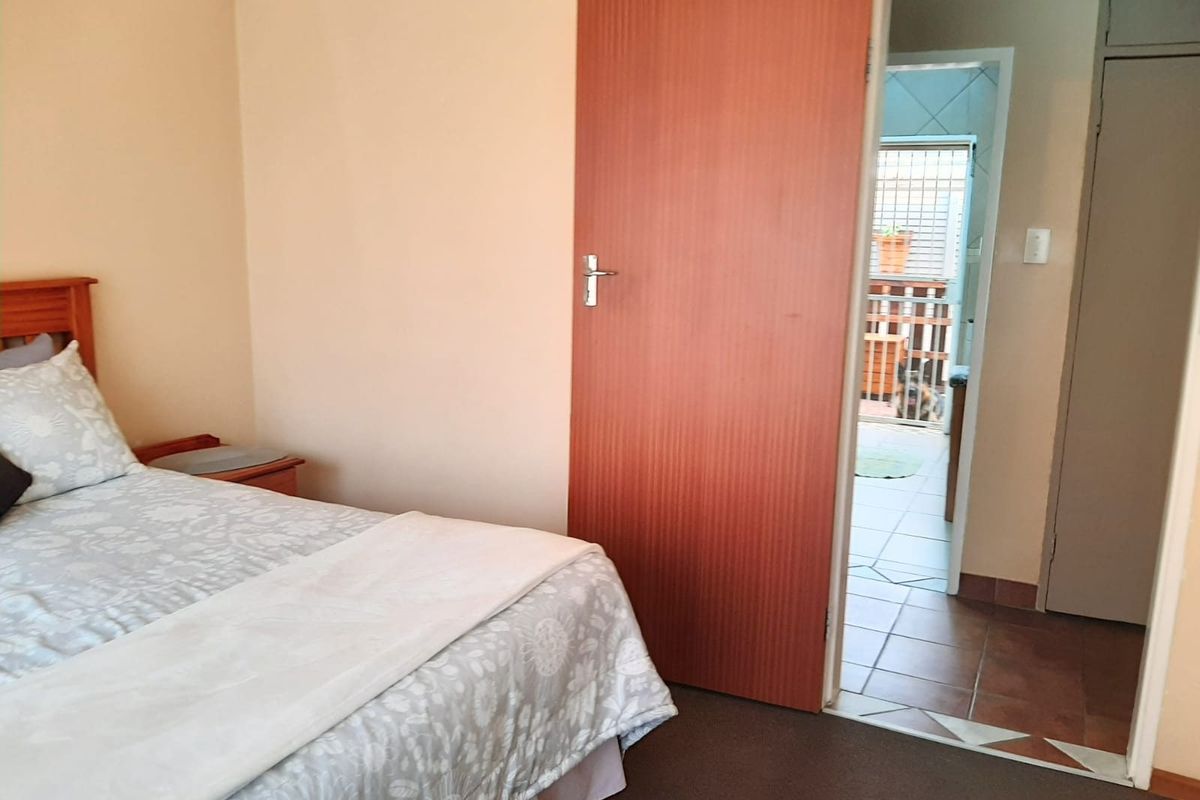 A bedroom featuring carpeted flooring and an internal door leading to an adjacent tiled area with built-in storage.