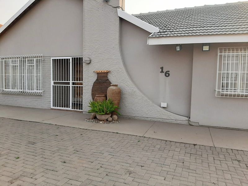 Front elevation of a residential property featuring a paved driveway, textured facade, and secure window bars.